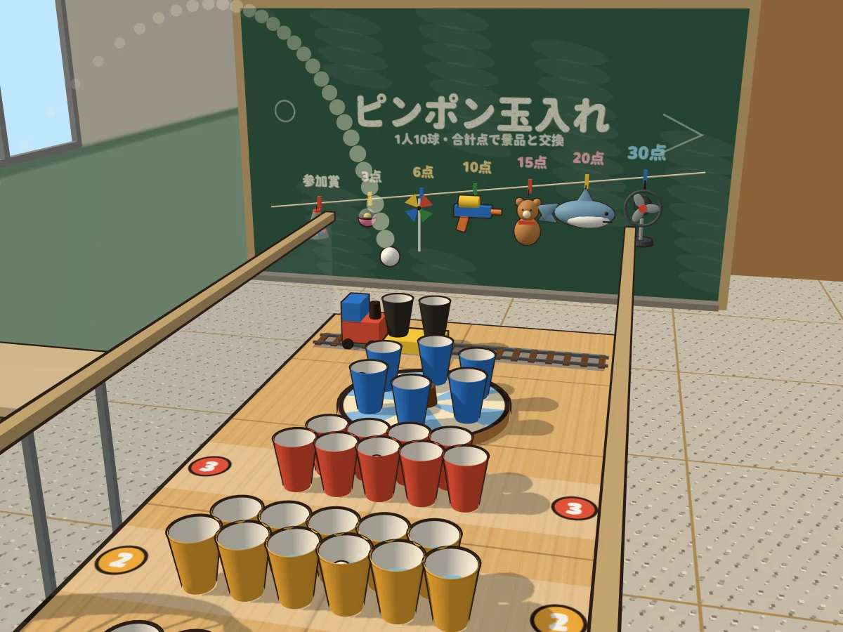 遊戲畫面:教室裡用課桌拼成的乒乓球攤,由前到後排著黃杯、紅杯、轉盤上的藍杯和小火車載著的黑杯;一顆乒乓球拖著一串點狀軌跡從左上方落下,正要掉進杯子裡,後面的黑板寫著「ピンポン玉入れ」,景品從參加獎一路掛到 30 分的電風扇